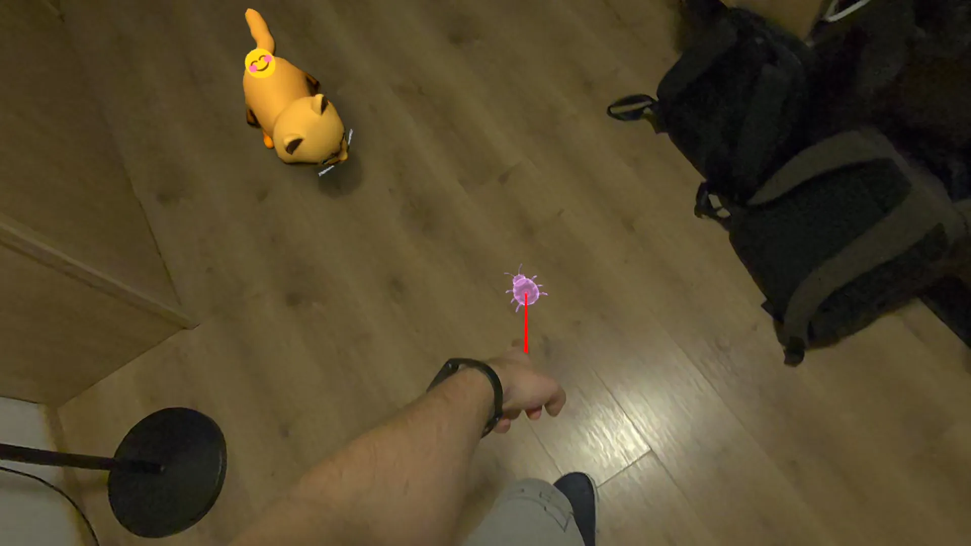 The player points at a glowing holographic critter on a real floor while an orange tabby cat runs in to pounce